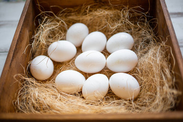 Eco-product. A wooden box of hay containing a ten white eggs. View from the top. Close up. White background. Concept of natural and eco-friendly food