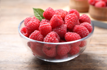 Delicious fresh ripe raspberries in bowl on wooden table, closeup