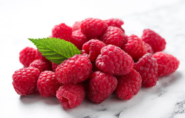 Delicious fresh ripe raspberries with green leaf on white marble table, closeup