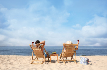 Couple with wine on sunny beach at resort