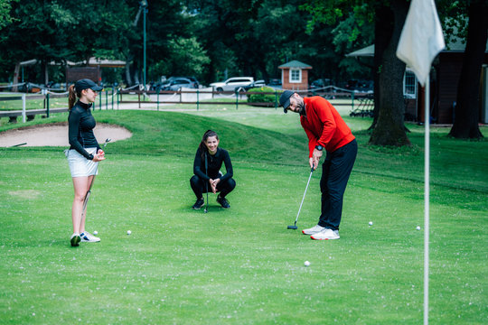 Golf putting lesson, two young female golfers practicing putting with golf instructor
