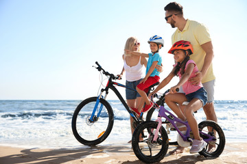 Obraz premium Happy parents teaching children to ride bicycles on sandy beach near sea