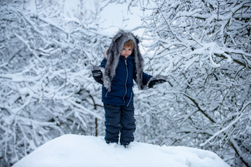 Fototapeta na wymiar Little Santa going in the winter on snow-covered field. Children in winter park. Little child boy walking in winter field.
