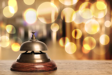 Wooden table with hotel service bell on blurred background. Space for text