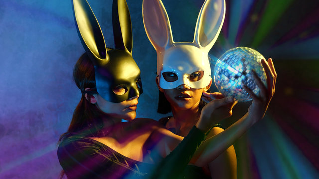 Portrait of two young cute Asian women in black and white rabbit mask posing with small disco ball on the neon lights
