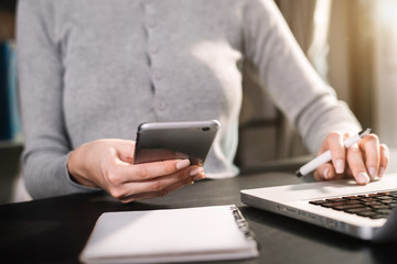 Businessman use smartphone and take notes in the notebook at the office desk in the morning.