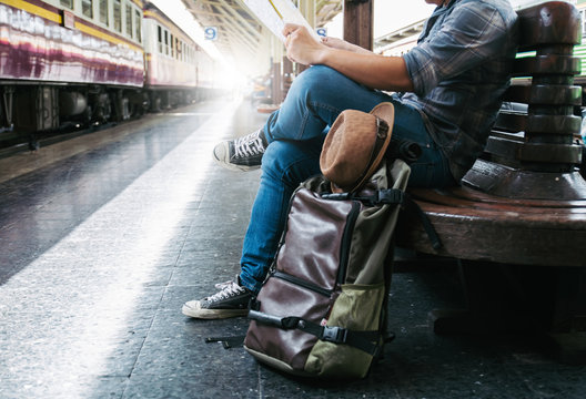 Side Portrait Of A Young Man Traveler Sitting With Map Choose Where To Travel And Bag Waiting For Train At Train Station, A Young Man Traveler Sitting With Map 