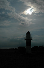 A small lighthouse seen in backlight with a sinister sky as background.