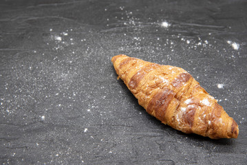 One croissant lies on a black slate background.