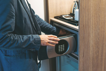 Adult man in blue jacket uses safe in the hotel room - obrazy, fototapety, plakaty