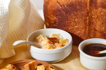 Square toasted pieces of homemade delicious rusk, hardtack, Dryasdust, zwieback, bread, Liquid honey and plate with milk in a white plate on a white tablecloth.
