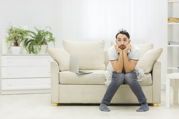 Fototapeta na wymiar Young single father overwhelmed with household chores sitting on sofa in living room.