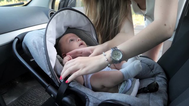 Young mother putting her baby boy on a safety child car seat
