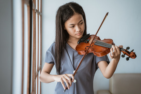 close up of teenage girl learn to play a violin instrument beside the window in a room at home
