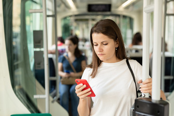 Young woman browsing and typing messages on phone on way to work in modern streetcar ..