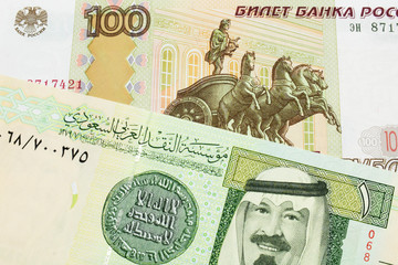 A macro image of a Russian one hundred ruble note paired up with a green and yellow one riyal bank note from Saudi Arabia.  Shot close up in macro.
