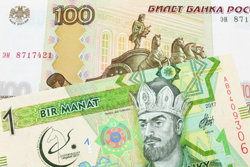 A macro image of a Russian one hundred ruble note paired up with a green and yellow one manat note...