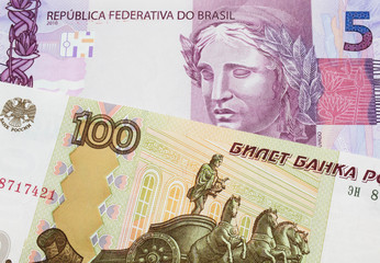 Fototapeta premium A macro image of a Russian one hundred ruble note paired up with a pink and purple five real bank note from Brazil. Shot close up in macro.