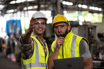 Two industrial Engineers and Technician workers with helmet or hardhat working and checking machinery on notebook or laptop in industry manufacturing Factory