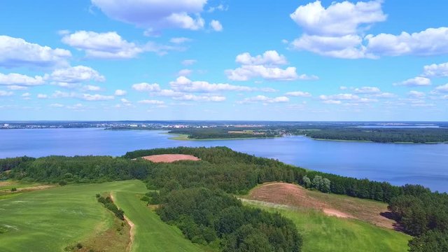 The drone descends smoothly with a beautiful view of the lake, blue sky and green field.
