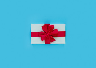 Pink gift box with red bow and ribbon on blue paper background with empty place for text.