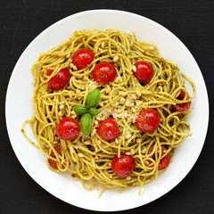 Homemade Pesto Pasta with Tomatoes and Pine Nuts on a black surface, top view. Flat lay, overhead, from above. Close-up.