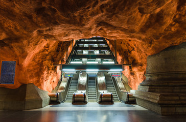 Sweden, Stockholm, May 30, 2018: underground metro tunnelbana station Radhuset (blue line, central station) with escalator and orange brown patterned caves walls and ceiling - modern art gallery