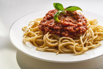 Traditional pasta bolognese served on a white plate and garnished with basil