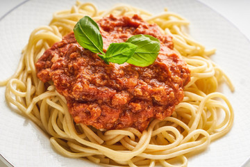 Traditional pasta bolognese served on a white plate and garnished with basil