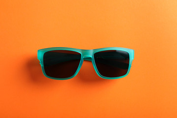 Stylish sunglasses on orange background, top view