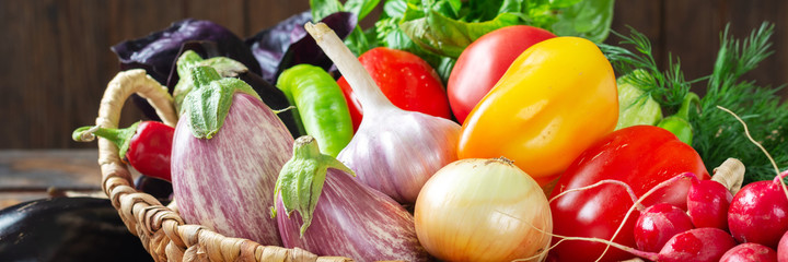 Assortment of vegetables in a basket on the table. A lot of different raw vegetables in the basket. Eggplant, tomatoes, garlic, sweet pepper, onion on the table. Healthy food concept. Banner