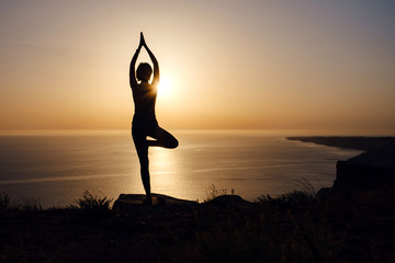 The woman with yoga posture on the mountain at sunset