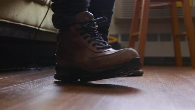 A man putting on a pair of leather boots, tying up the shoelaces, and then walking out of frame. Slow-motion, low-angle close up of brown leather boots and his hands.