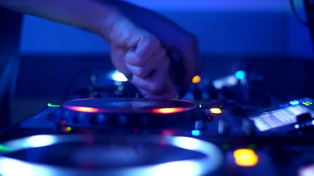 DJ hands on CDJ in nightclub turning and pushing buttons, and scratching