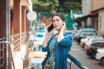 An elegant woman in summer clothes is talking on the phone straightening her hair. Street with cars in the background. Concept of communication and social networks