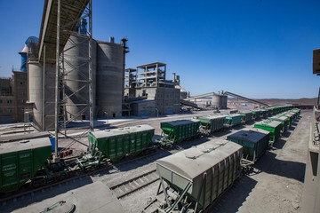 Mynaral/Kazakhstan: Modern cement plant in desert. Hopper cars on loading railroad terminal. Cement silo on blue sky background.