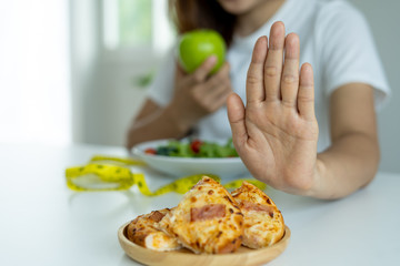 Obraz na płótnie Canvas Women are rejecting and pushing pizza and eating apple, vegetable salads placed in front of them. Women are choosing foods that are healthy for the body.