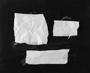 Obraz premium White blank paper scraps with transparent tape on black chalkboard, blackboard background and texture