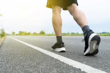 The legs of male athletes in black shoes are preparing to run on the paved road Outdoor exercise for weight loss and good health.Fitness and healthy lifestyle Competition and successful concept.