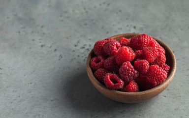 Fresh ripe raspberries in a wooden bowl on a gray background. The concept of healthy eating. Copy...