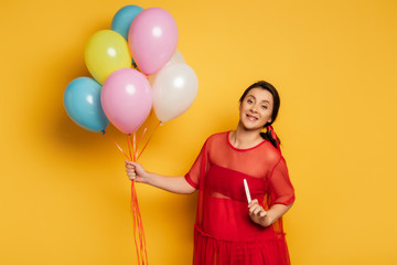 pregnant woman holding multicolored festive balloons and pregnancy test on yellow background