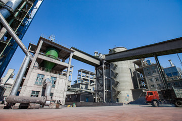 Mynaral, Kazakhstan: Grey tower and silo and industrial building of Jambyl Cement plant and red truck on clear blue sky background.