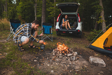 couple sitting near campfire. man cooking on fire. hiking concept