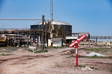 Fototapeta premium Old rusted oil storage tank and broken railway sign on old soviet factory (plant) against blue sky background.