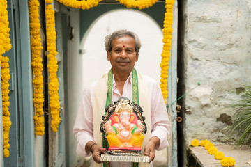 happy Elder man with Ganesha Idol coming home during ganesha or vinayaka Chaturthi festival -...