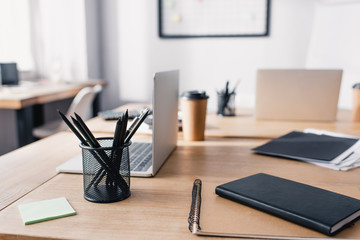 Selective focus of notebooks, stationery and laptops on wooden table in white office