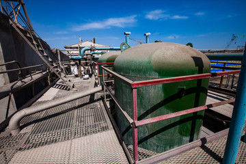 Green metal tanks, valves and other equipment on mesh (grid) floor. Abstract view of chemical plant. Blue sky background.