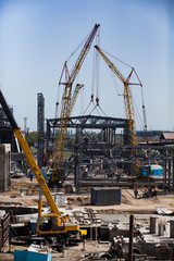 Fototapeta na wymiar Yellow mobile cranes and assembling metal structure of industrial building. Construction and Modernization of fertilizers plant.
