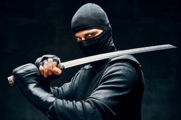 Fighting ninja posing with a sword over black background