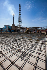 Modernization of outdated phosphate fertilizer plant. Industrial building construction. Workers assembling steel reinforcement of basement. Industrial building and blue sky on background.